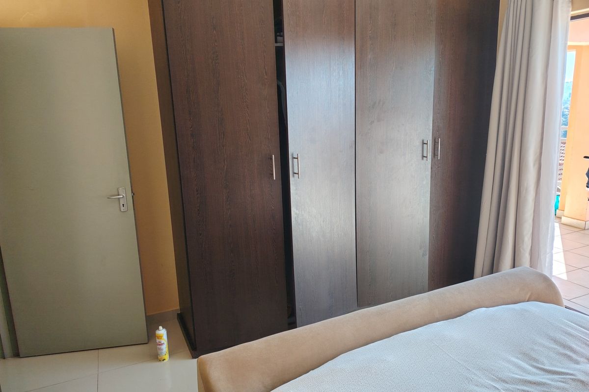 A bedroom featuring dark wood built-in wardrobes and tiled flooring, with direct access to an outdoor balcony area.