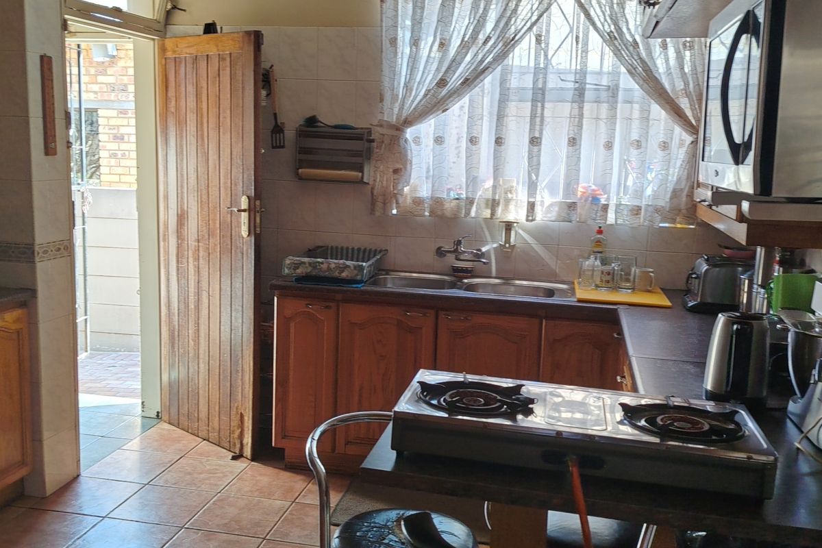 A functional kitchen featuring wooden cabinetry, tiled flooring, a double sink, and direct access to the exterior.