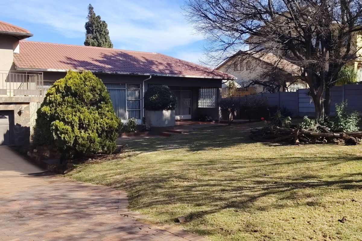 Rear view of the property featuring a tiled roof, paved driveway, and a spacious garden area with established trees and boundary walling.
