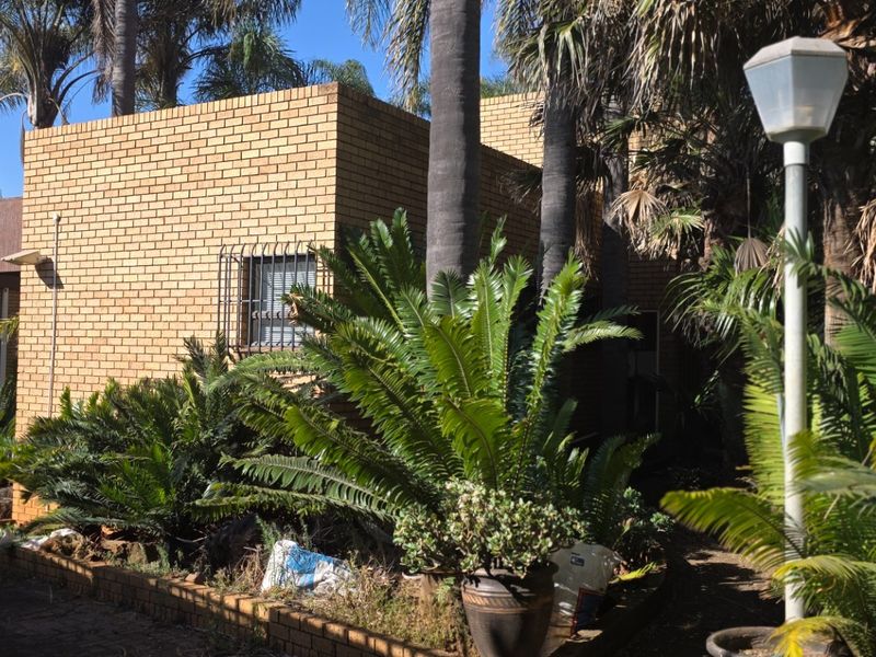 A view of the property's rear exterior featuring face brick walls, security bars on windows, and an established garden with mature trees.