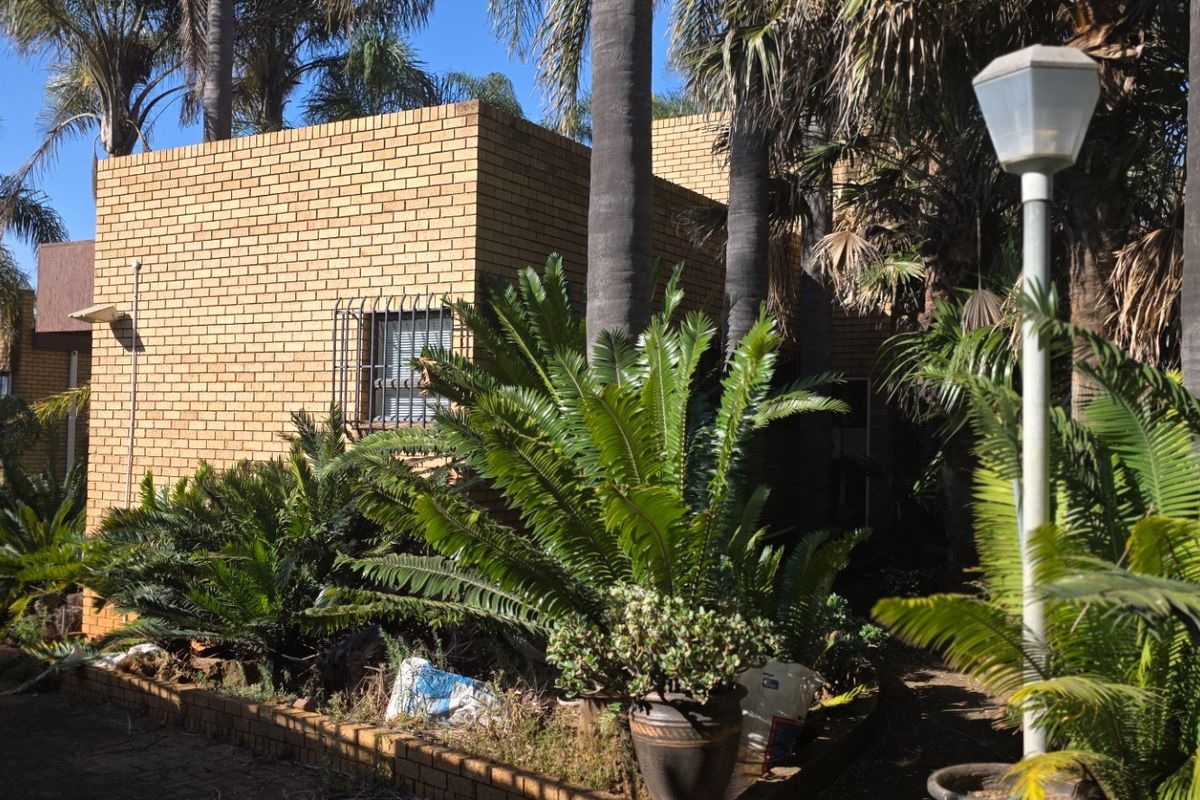 A view of the property's rear exterior featuring face brick walls, security bars on windows, and an established garden with mature trees.
