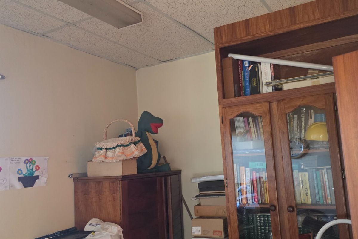 A bedroom space featuring acoustic ceiling tiles and a fluorescent light fixture, currently used for storage.