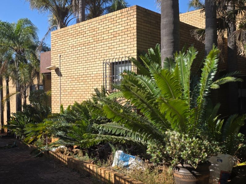 A view of the rear exterior featuring a face brick facade, security bars on windows, and a paved driveway area with established garden landscaping.