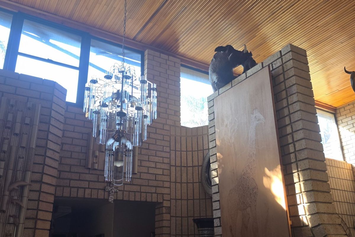 Spacious living area featuring distinctive exposed brick walls, a warm timber slat ceiling, and a large feature chandelier.
