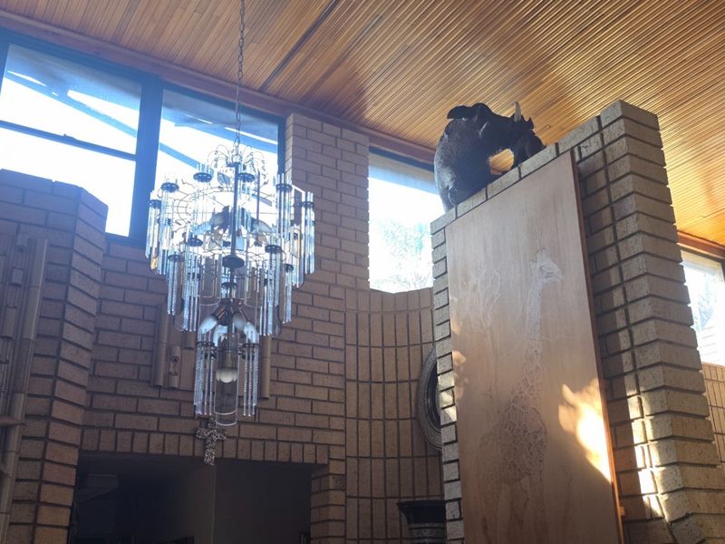 Spacious living area featuring distinctive exposed brick walls, a warm timber slat ceiling, and a large feature chandelier.