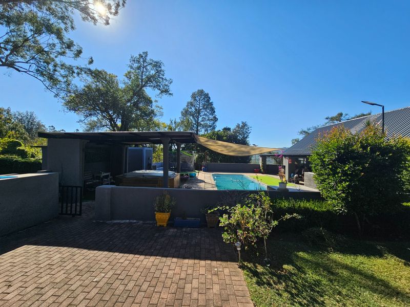 Outdoor entertainment area featuring a swimming pool, covered patio space, and paved surroundings, set within a landscaped garden environment.