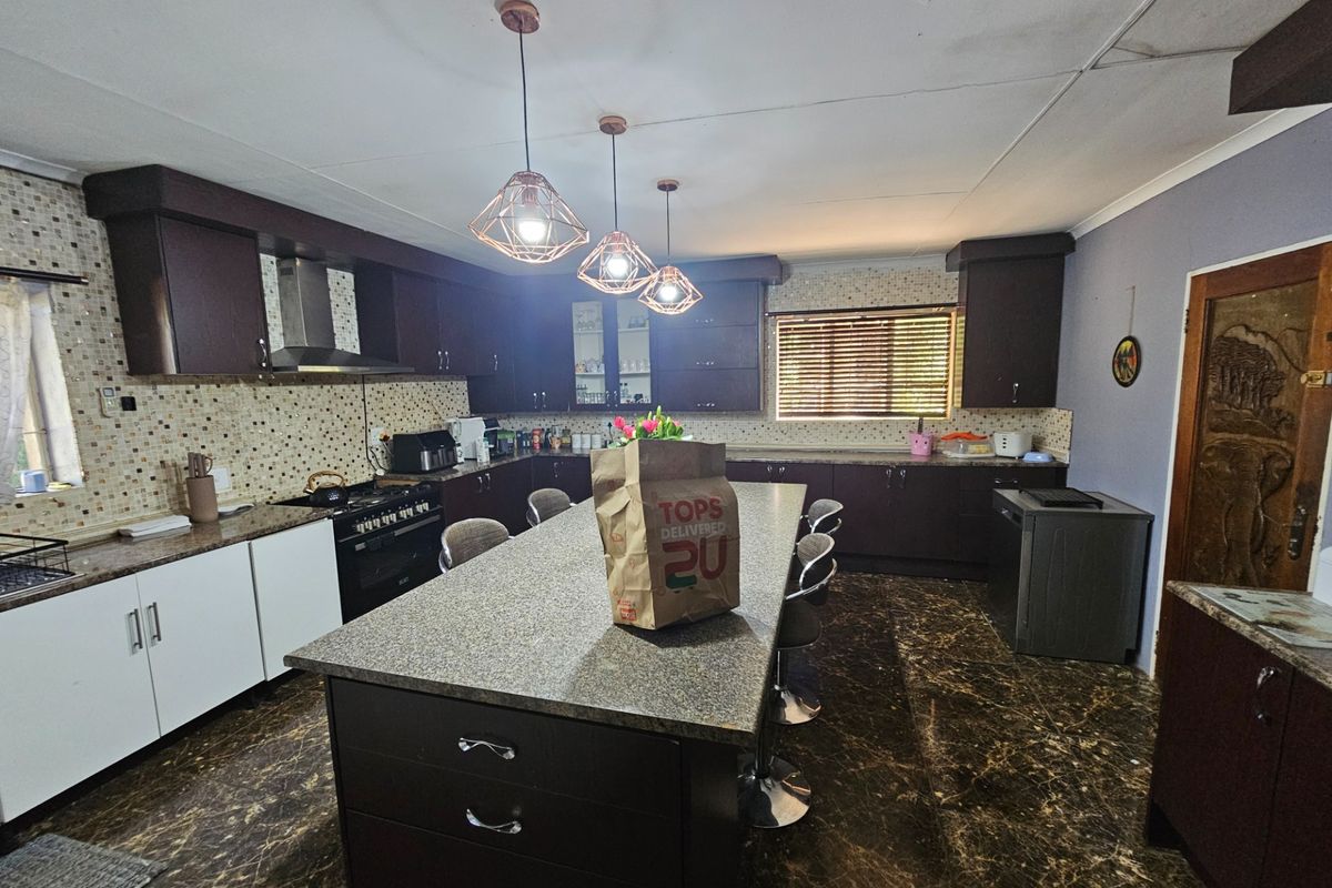 Spacious kitchen featuring a large central island, dark cabinetry, granite countertops, and a mosaic tile backsplash with integrated gas stove and extractor fan.