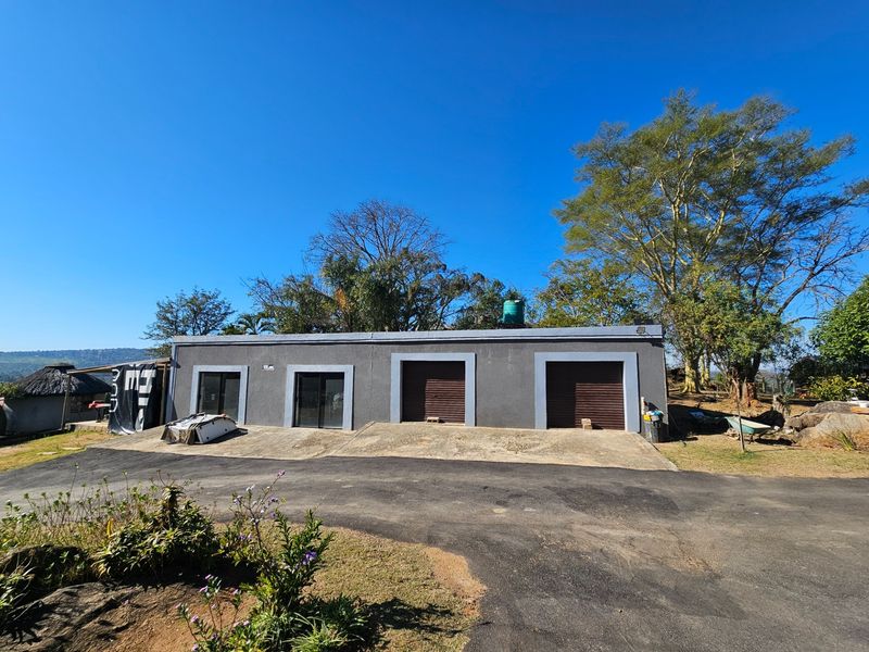 A multi-bay garage structure featuring roller shutter doors and sliding glass access points, situated on a paved driveway with an integrated water tank.