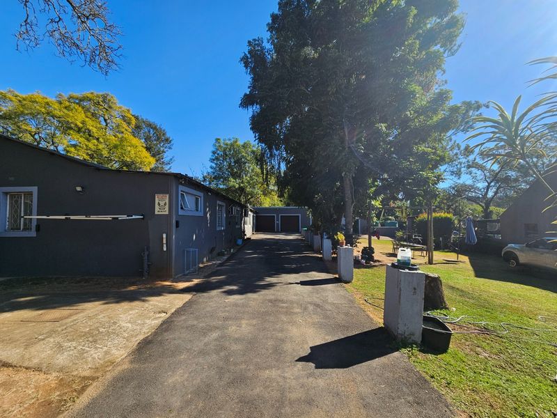 A wide asphalt driveway leading to a double garage on a small holding, featuring mature trees and established garden surroundings.
