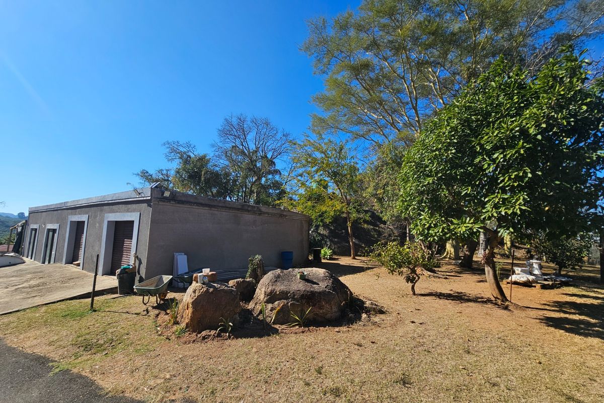 Rear exterior view of the property featuring a concrete driveway, roller shutter access doors, and a spacious garden with mature trees.