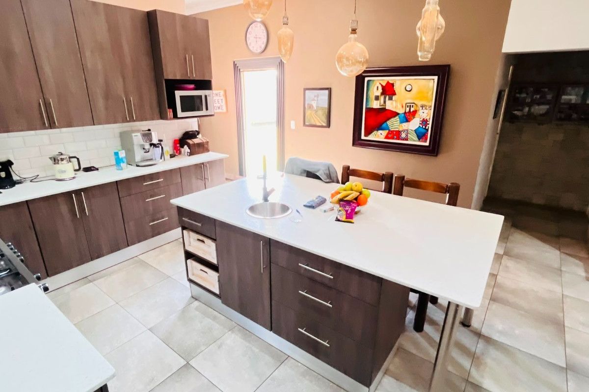 Modern kitchen featuring dark wood cabinetry, a central island with an integrated sink, white countertops, and subway tile backsplash.