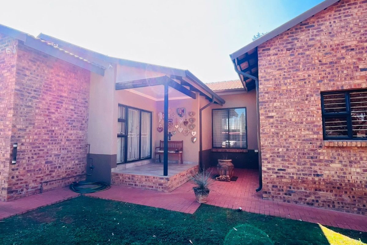 A rear view of the farm property featuring a face brick facade, a covered patio area, and a paved courtyard leading to the garden.