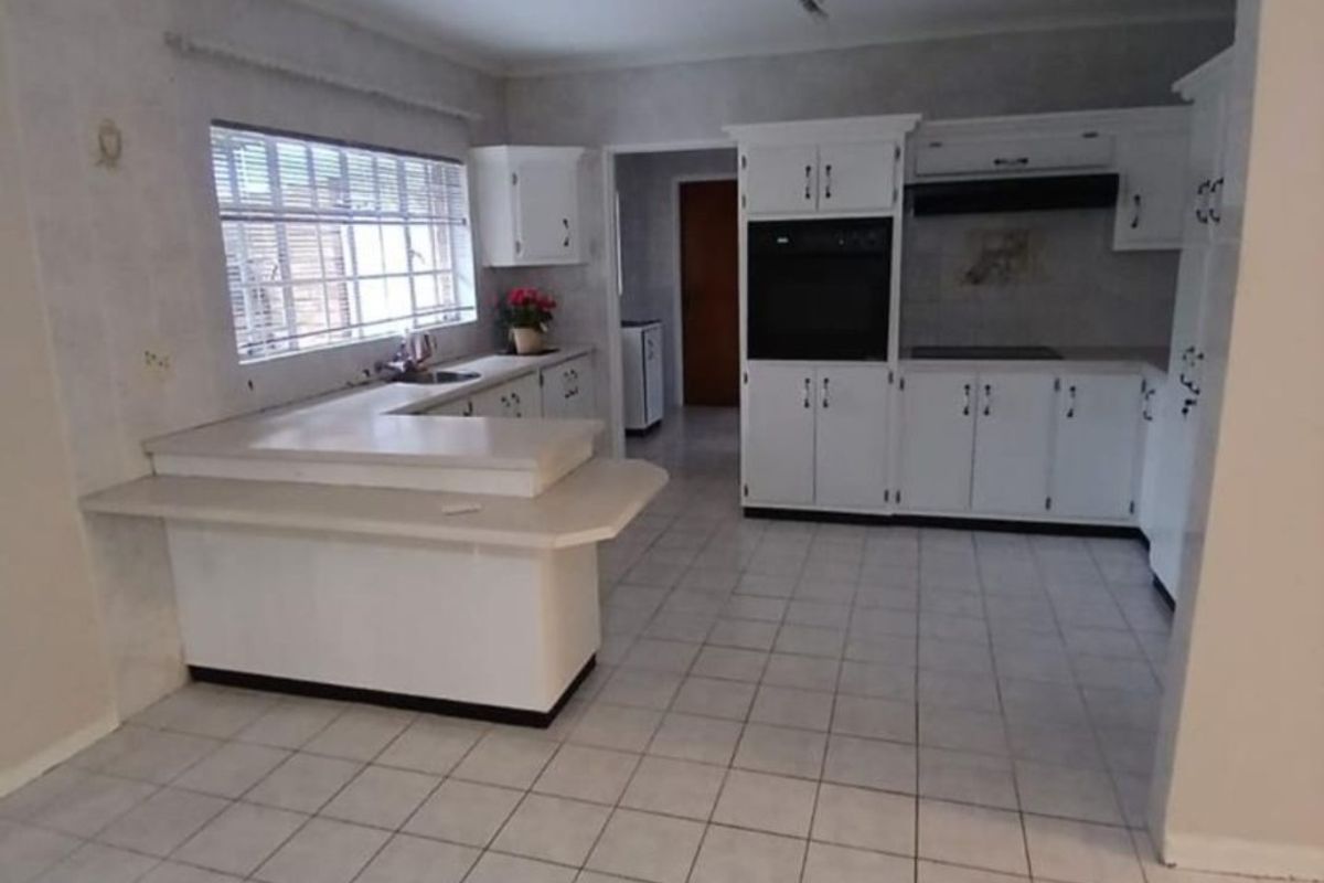 A functional kitchen featuring white built-in cabinetry, a breakfast bar, built-in oven, extractor fan, and tiled flooring.