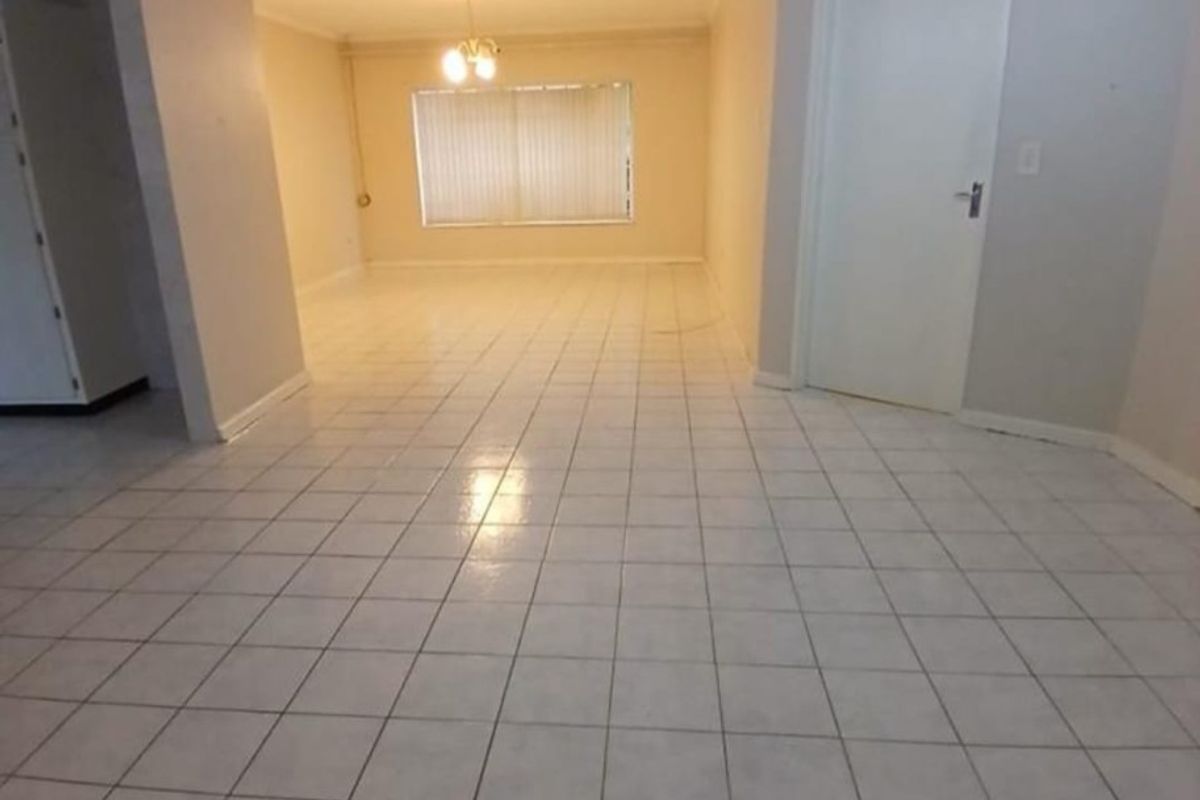A spacious, empty living area featuring neutral tiled flooring, clean walls, and natural light through vertical blinds.