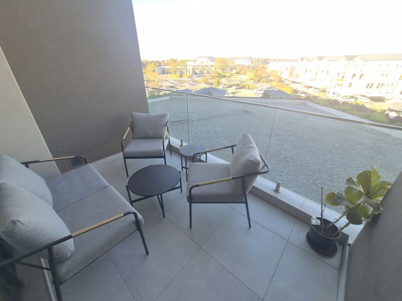 A modern balcony featuring a sleek glass balustrade and tiled flooring, offering an open view of the surrounding residential complex.