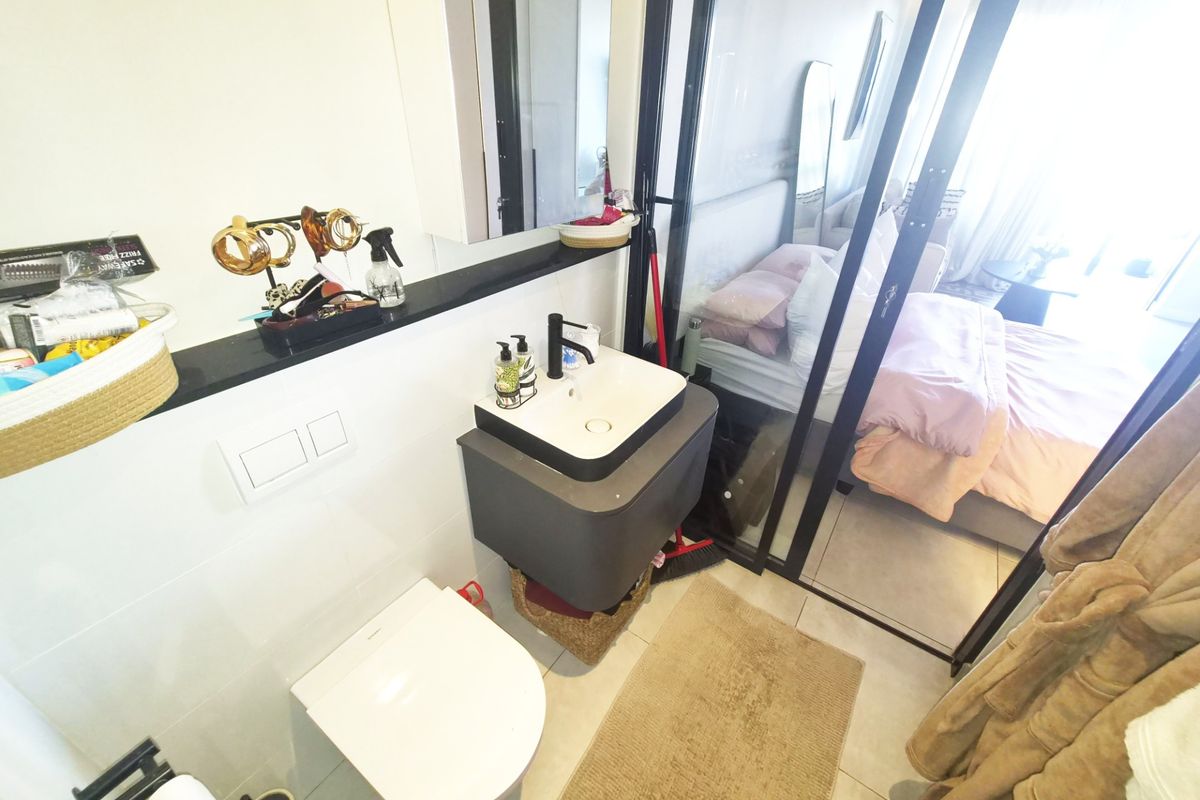Modern bathroom featuring a wall-mounted toilet, floating vanity with vessel sink, and a sleek glass partition separating it from the adjacent bedroom.