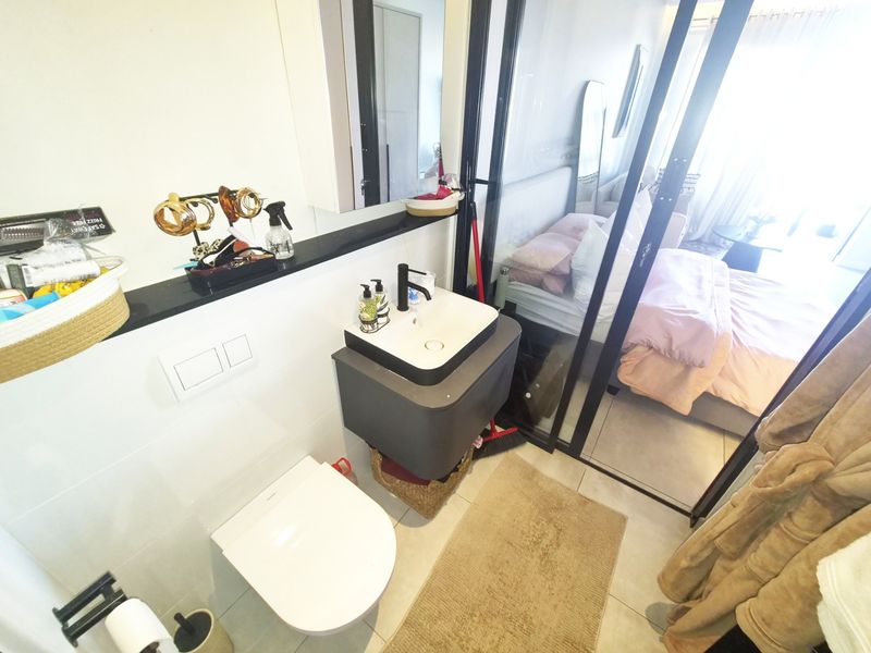 Modern bathroom featuring a wall-mounted toilet, floating vanity with vessel sink, and a sleek glass partition separating it from the adjacent bedroom.