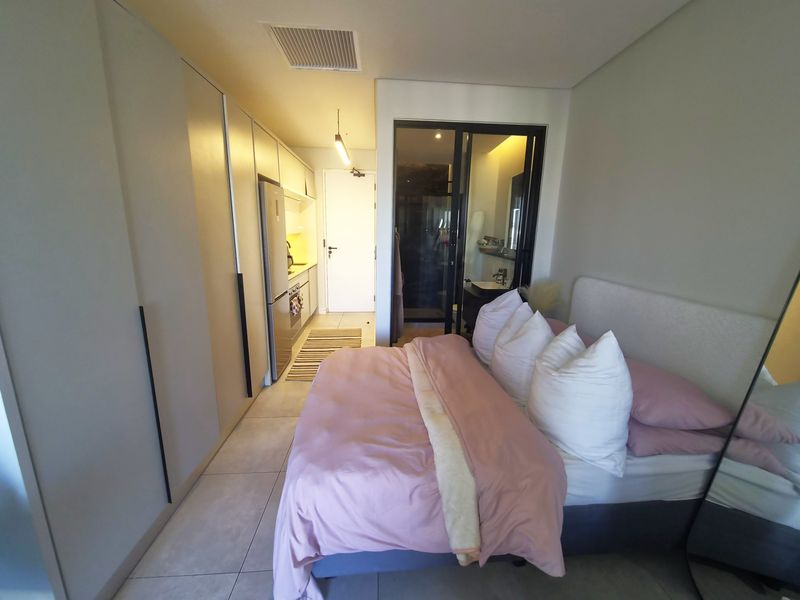 Modern open-plan studio apartment featuring a compact kitchen with built-in cabinetry, tiled flooring, and an adjoining en-suite bathroom.