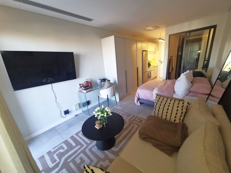 Modern open-plan studio apartment featuring tiled flooring, recessed ceiling lighting, and integrated kitchen cabinetry, creating a functional and cohesive living space.