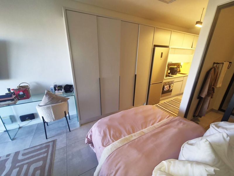 Modern open-plan studio apartment featuring a compact integrated kitchen with built-in cabinetry and sleek tiled flooring.