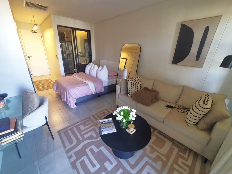 A modern open-plan studio apartment featuring tiled flooring, a combined living and sleeping area, and an integrated en-suite bathroom with a sliding glass door.