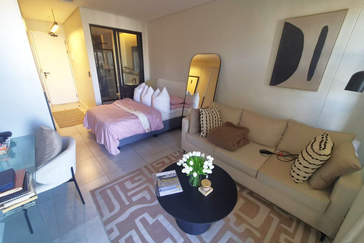 A modern open-plan studio apartment featuring tiled flooring, a combined living and sleeping area, and an integrated en-suite bathroom with a sliding glass door.