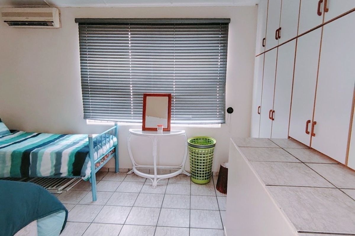 A bedroom featuring tiled flooring, built-in storage cupboards, a wall-mounted air conditioning unit, and venetian blinds.