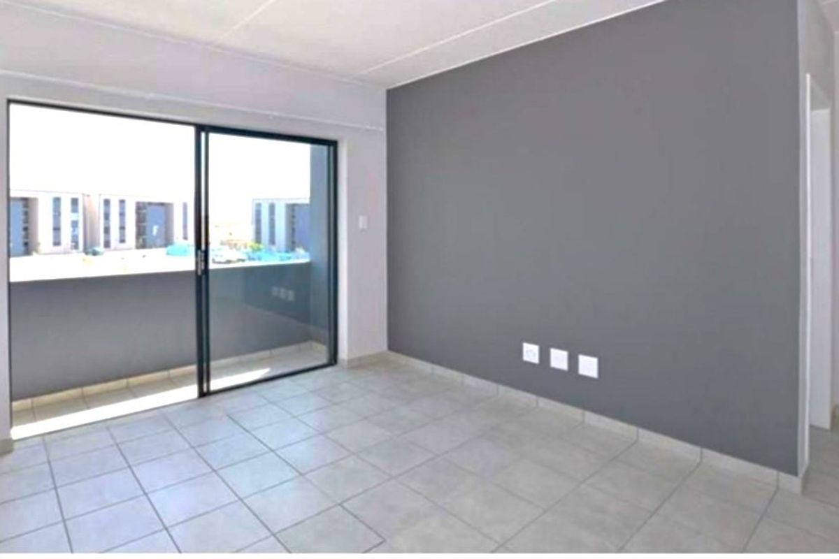 An empty living room featuring neutral tiled flooring, a grey accent wall, and a large sliding glass door providing access to a balcony.