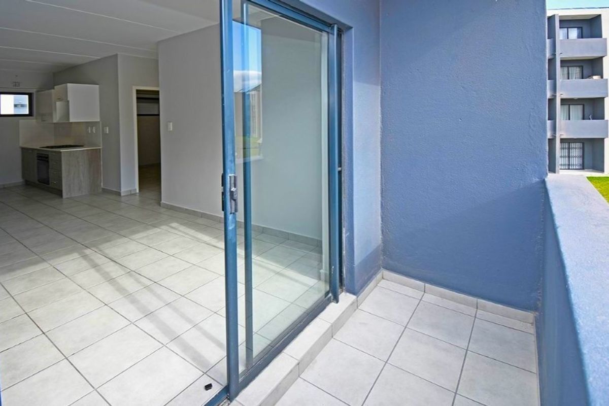 An open-plan living and kitchen area featuring tiled floors and a sliding door leading to a private balcony.