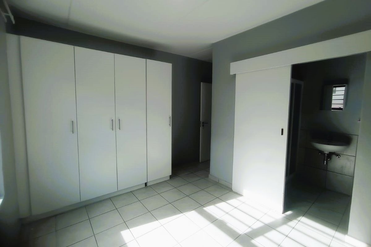 A clean, empty bedroom featuring built-in cupboards, tiled flooring, and a sliding door leading to an en-suite bathroom.