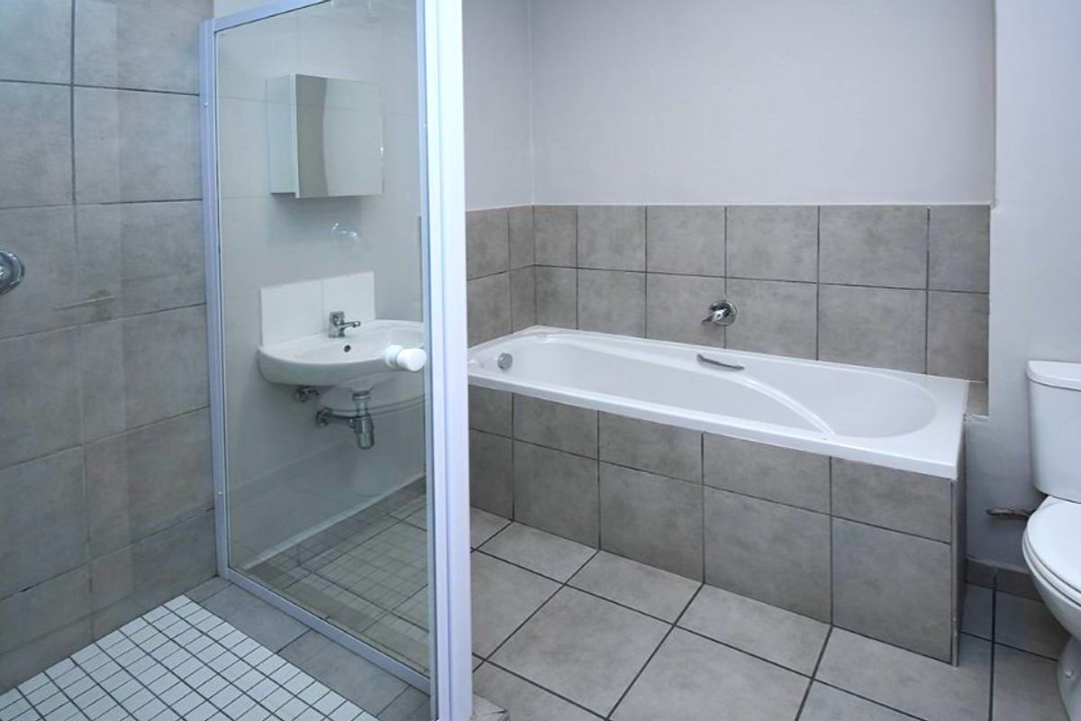 A clean, functional bathroom featuring a separate shower enclosure, bathtub, pedestal basin, and toilet with neutral grey tiling throughout.