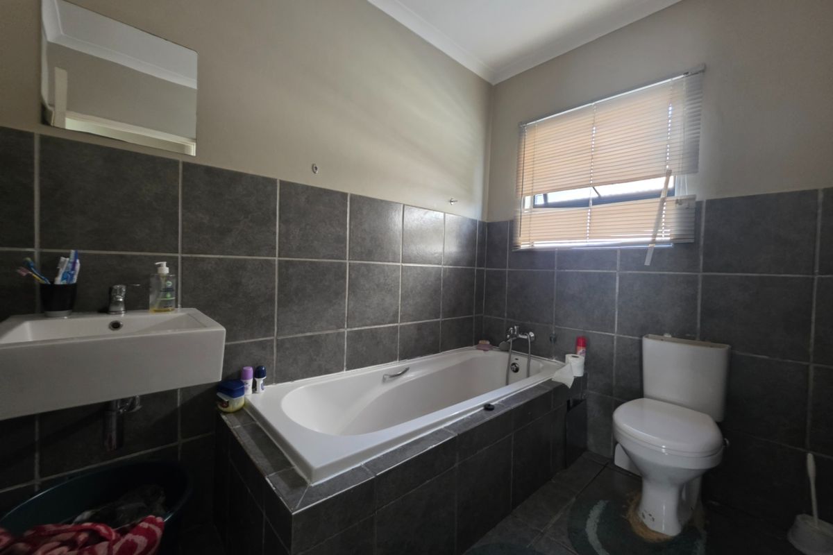 A functional bathroom featuring a built-in bathtub, wall-mounted basin, and toilet with dark grey wall tiling and neutral paintwork.