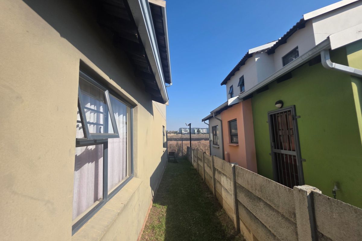 A narrow side passage between two townhouse units featuring precast concrete boundary walls, aluminium window frames, and exterior drainage systems.