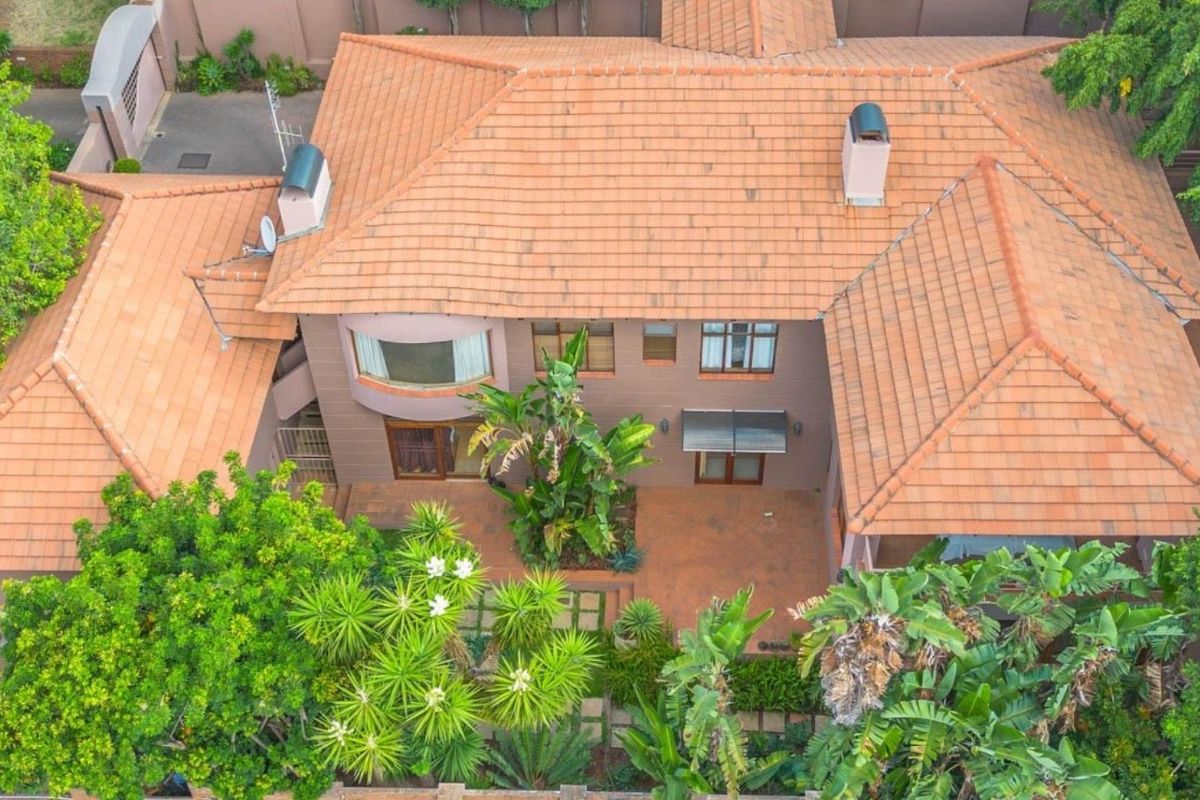 Aerial view of a residential property featuring a terracotta tiled roof, paved patio area, and established garden surroundings.