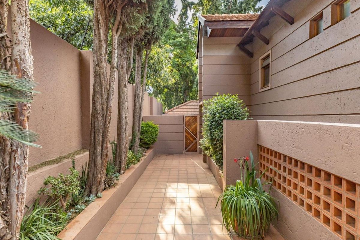 A well-maintained side walkway featuring tiled flooring, a decorative breeze block wall, and a secure timber gate leading to the rear garden area.