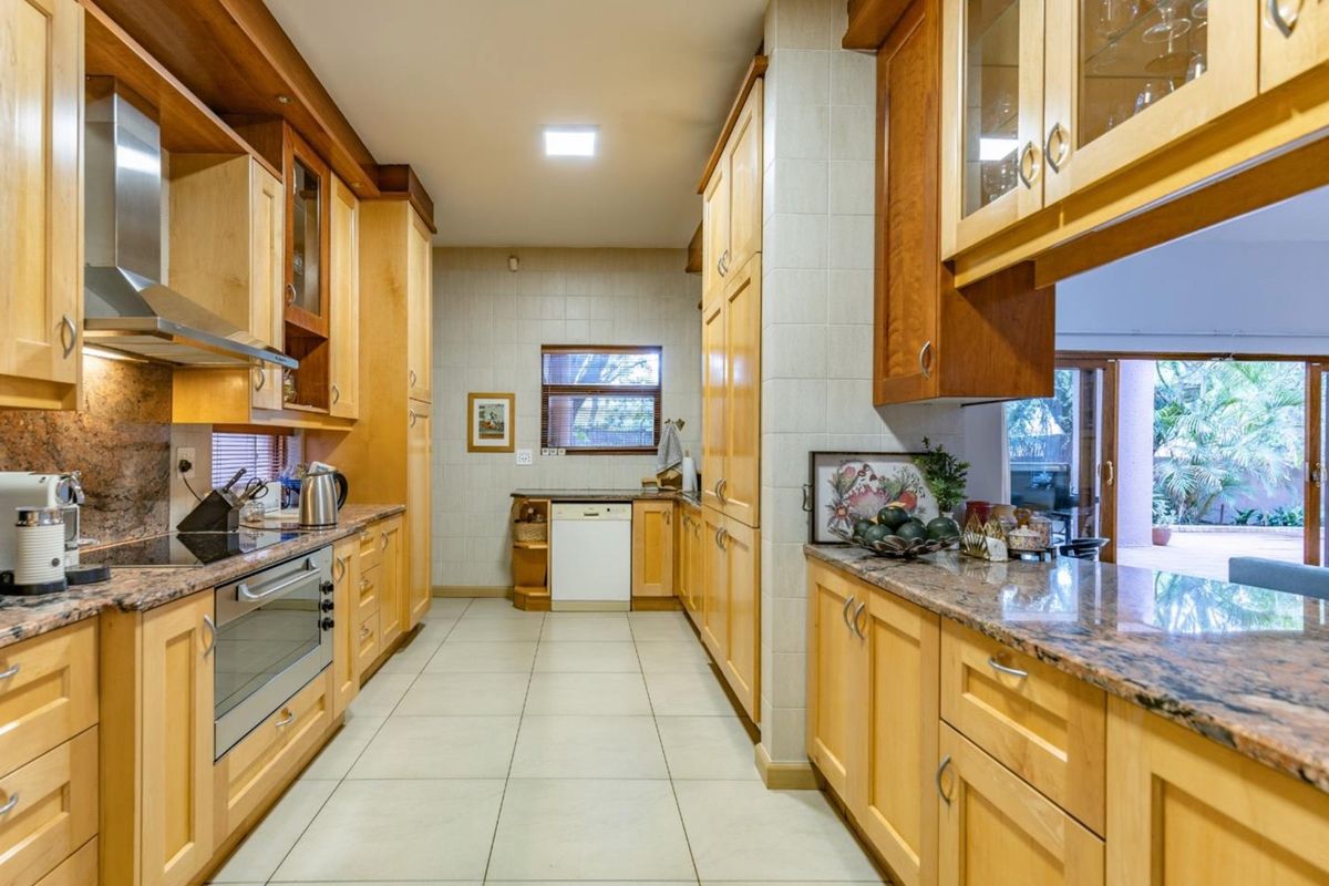 A well-maintained kitchen featuring light wood cabinetry, granite countertops, built-in appliances, and tiled flooring, with direct access to an outdoor patio area.