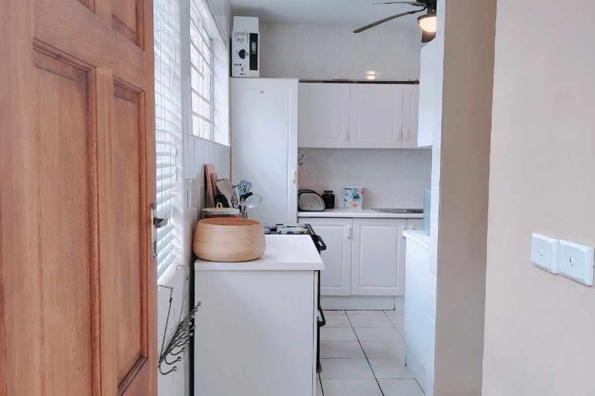 A compact kitchen featuring white cabinetry, tiled flooring, and a ceiling fan, offering a functional layout with potential for modern updates.