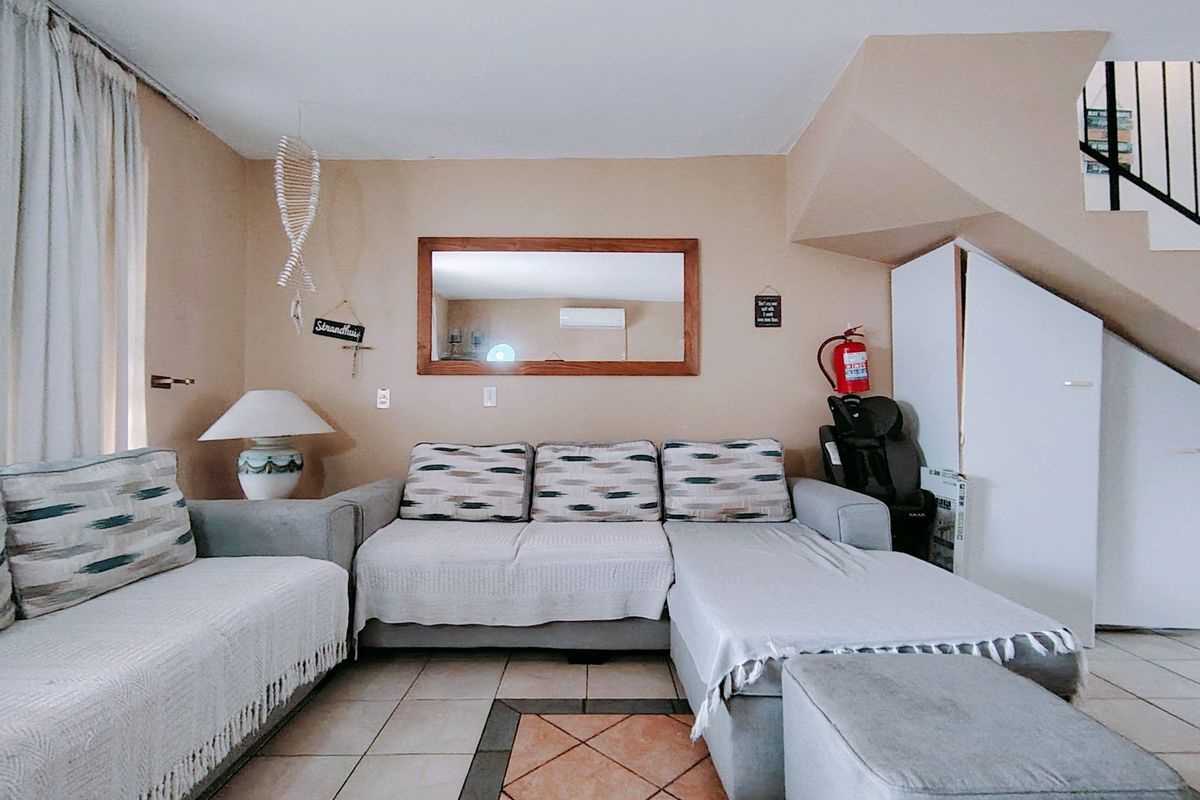 A comfortable living room featuring tiled flooring, an air conditioning unit, and convenient under-stair storage space.