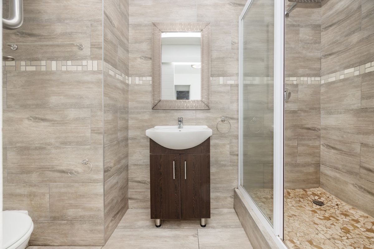 Modern bathroom featuring a vanity cabinet with basin, a glass-enclosed shower, and neutral wood-look wall and floor tiling.