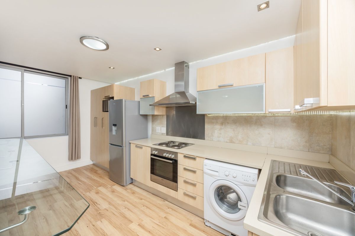 Modern kitchen featuring light wood cabinetry, stainless steel appliances, integrated hob and oven, and a double sink with tiled splashback.