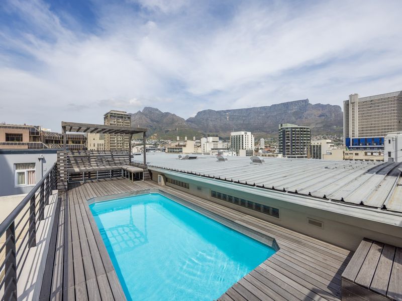Rooftop terrace featuring a swimming pool, timber decking, and a pergola, offering expansive city and mountain views.