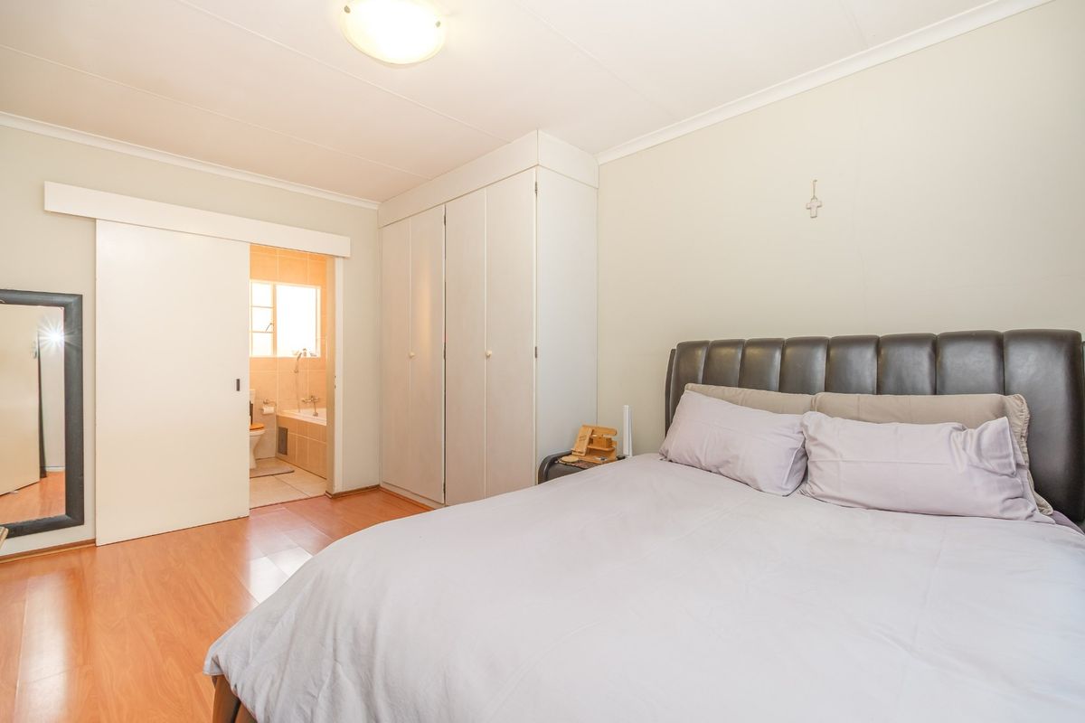 A well-lit bedroom featuring laminate flooring, built-in cupboards, and direct access to an en-suite bathroom.