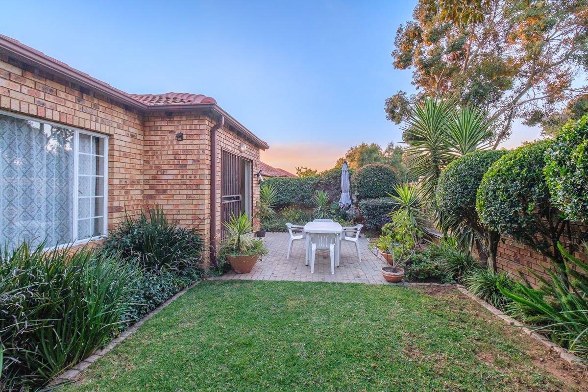 A well-maintained rear garden featuring a paved patio area, established landscaping, and a brick-faced exterior wall.
