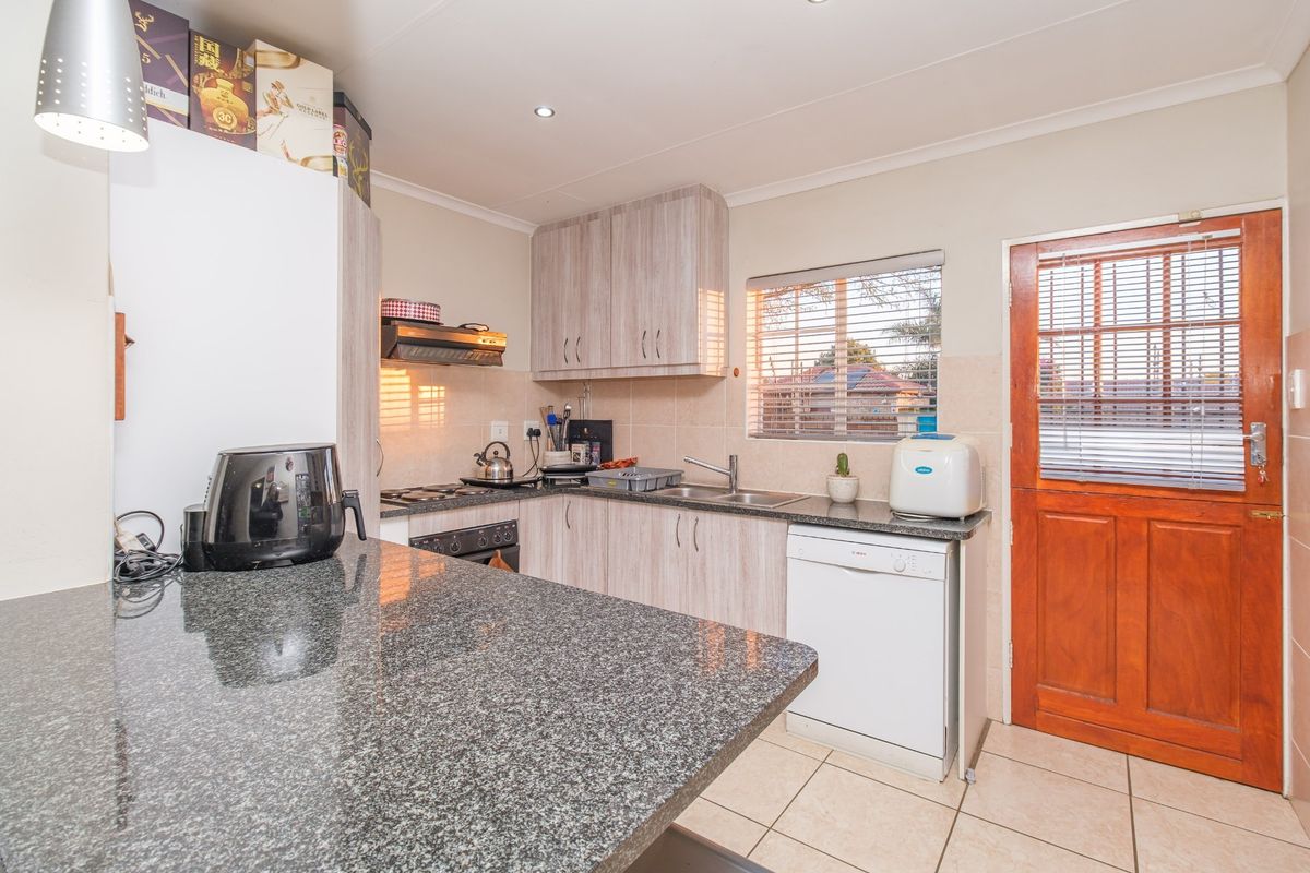 Functional kitchen featuring granite countertops, light wood-finish cabinetry, gas hob, extractor fan, and direct access to the exterior via a timber door.