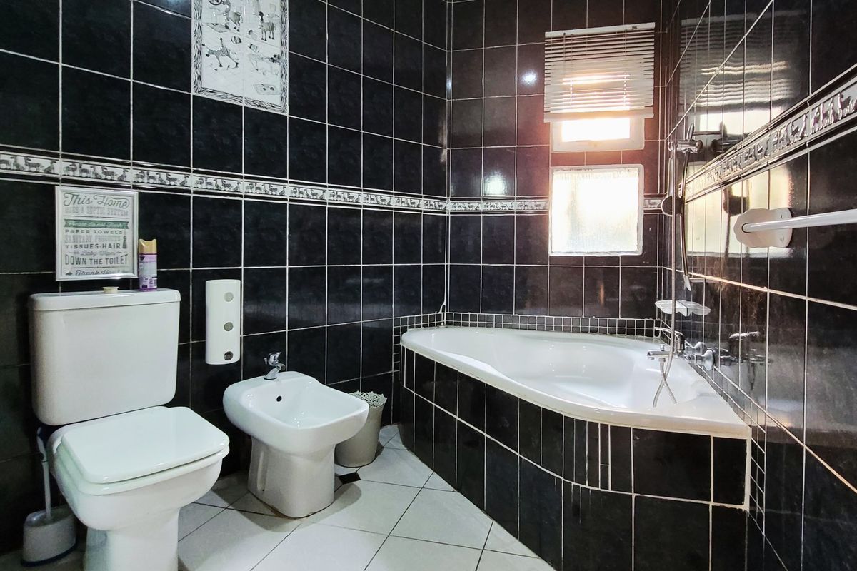 A bathroom featuring dark tiled walls, a corner bathtub, a bidet, and a toilet, offering a functional layout with classic finishes.