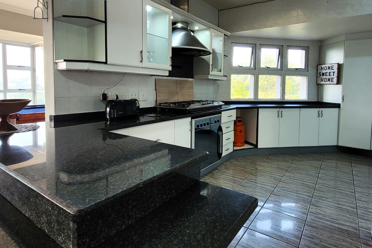 A functional kitchen featuring dark granite countertops, built-in cabinetry, a gas hob with extractor fan, and tiled flooring with natural light.