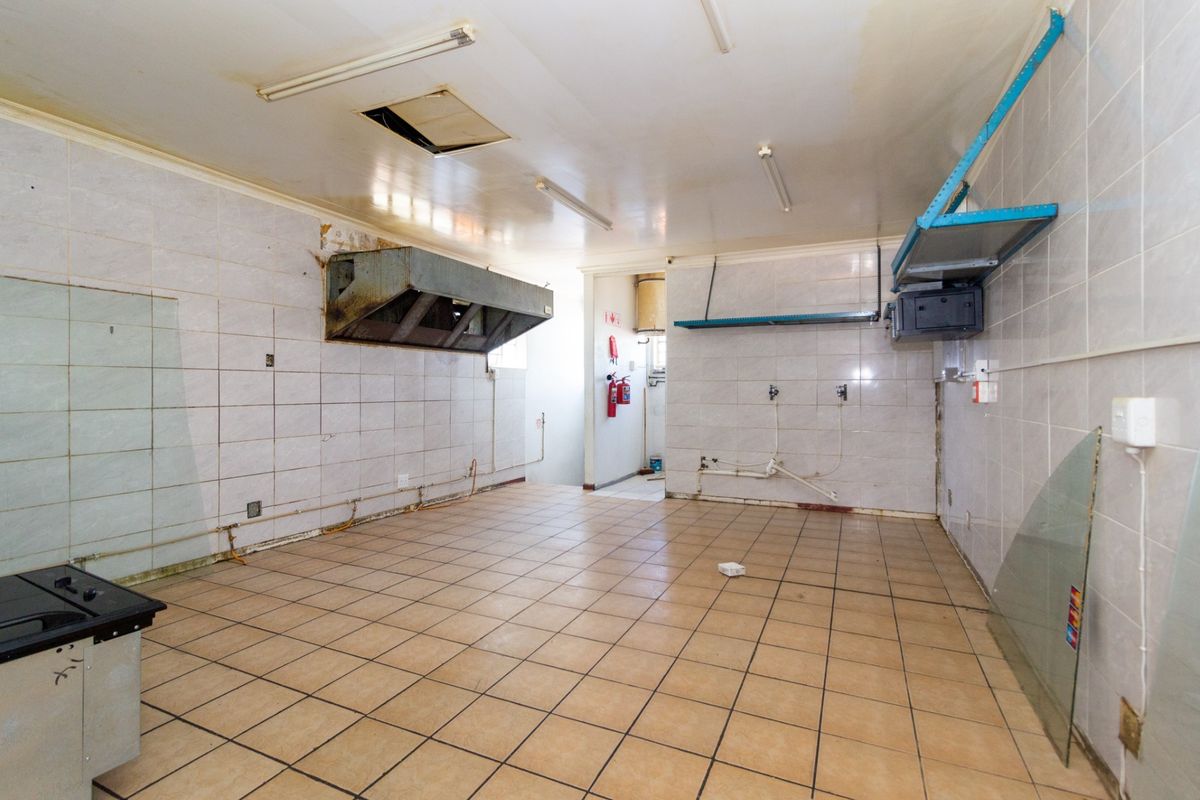 A vacant commercial kitchen space featuring tiled walls and floors, an extractor hood, and basic utility connections, requiring renovation and refurbishment.