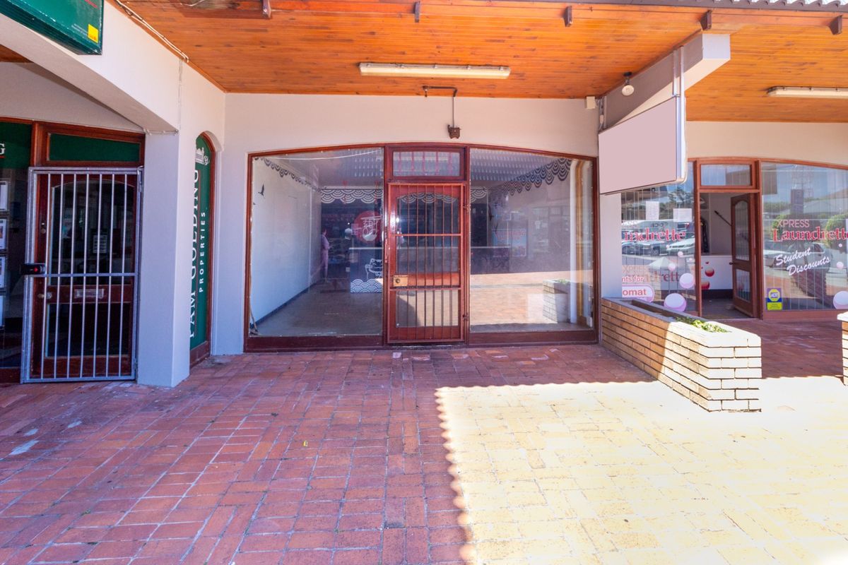 Front facade of a retail unit featuring a glass storefront, security gate, and covered brick-paved entrance area.