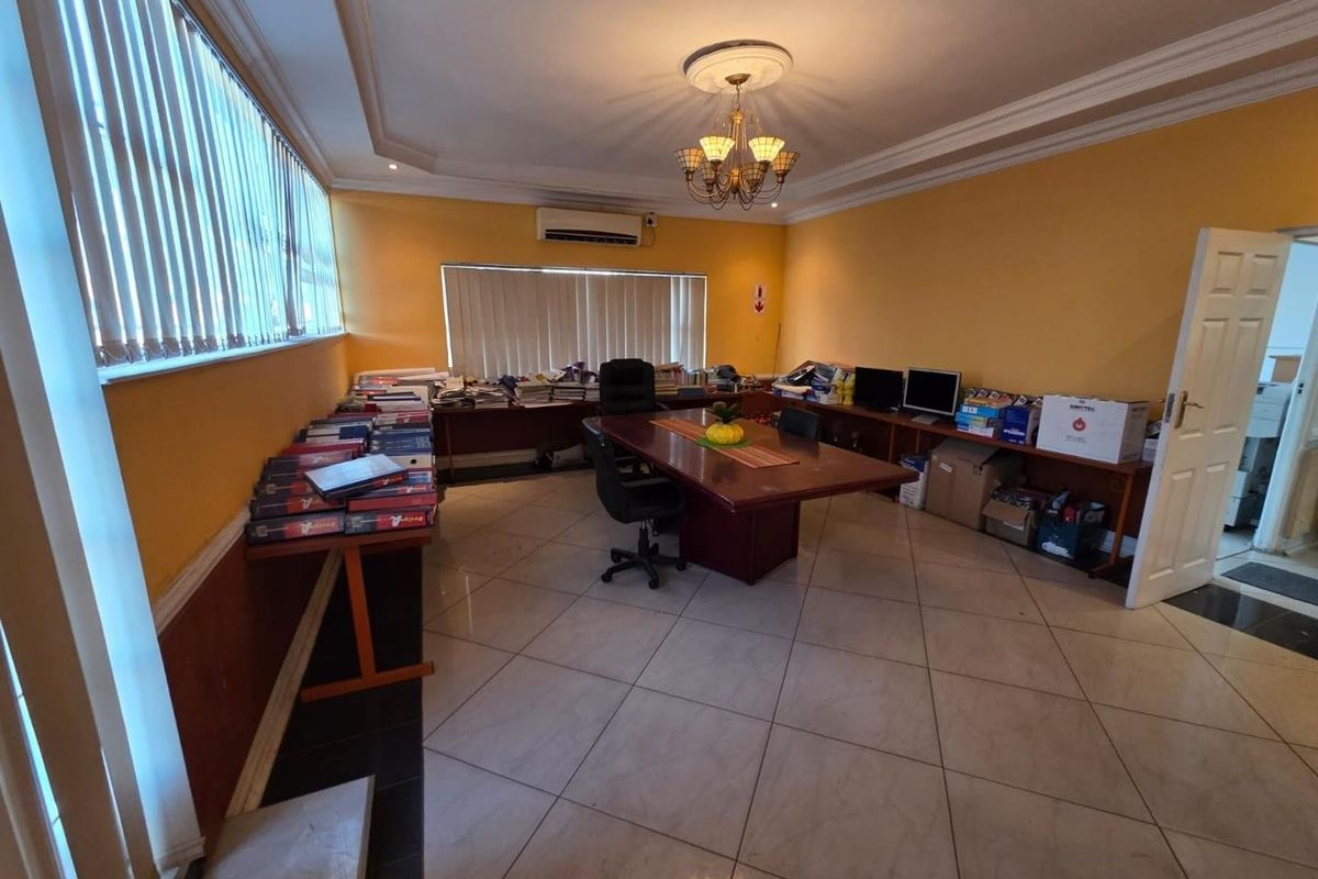 A spacious office area featuring tiled flooring, coved ceilings, a central chandelier, and built-in shelving units along the walls.