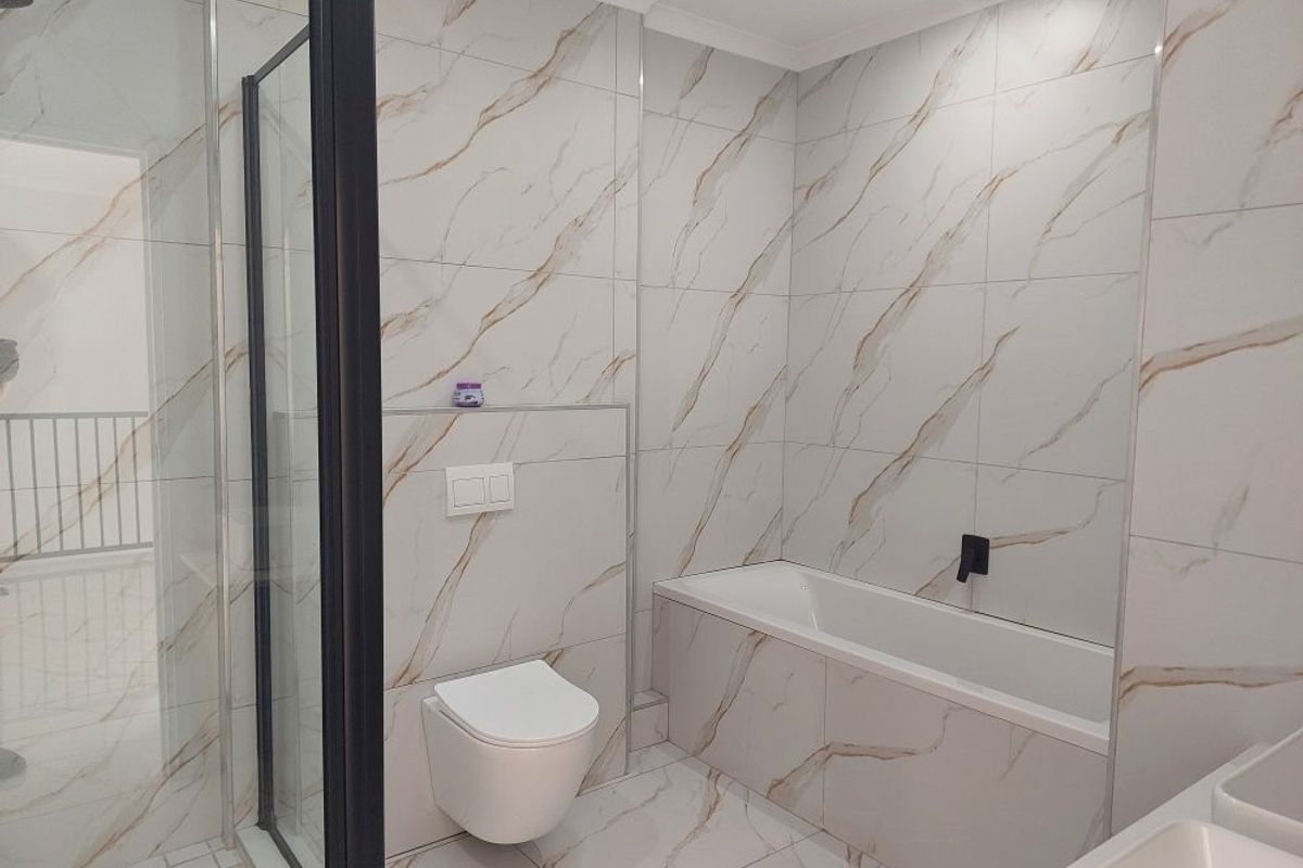 Modern, renovated bathroom featuring marble-look wall tiles, a walk-in shower with black frame, wall-hung toilet, and a built-in bathtub.